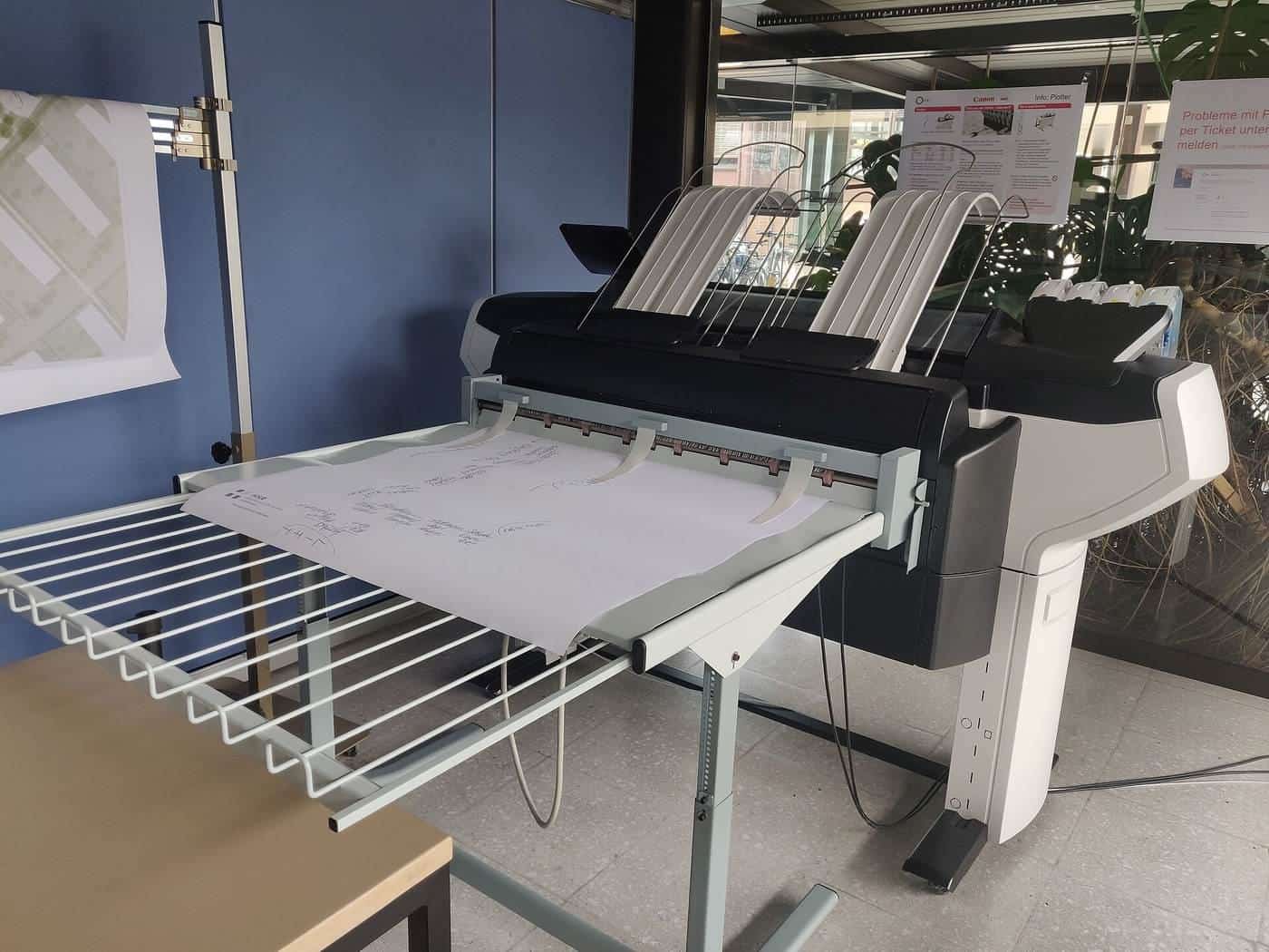 A large-format printer with paper output trays in a print room